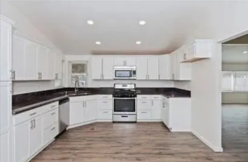 Modern white kitchen with black countertops and wooden flooring.