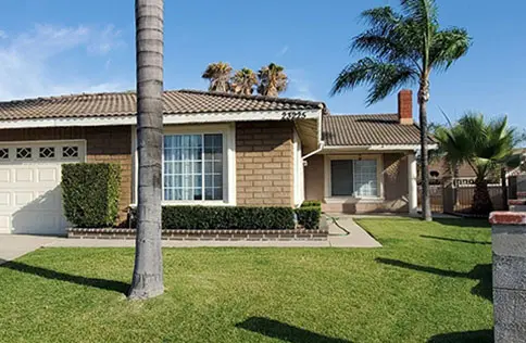 Single-story suburban house with a manicured lawn and palm trees.