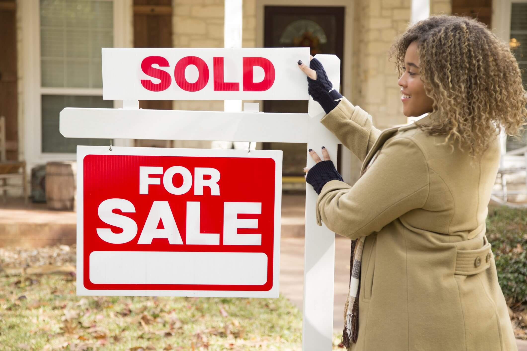 Woman placing "SOLD" sign on for-sale sign.