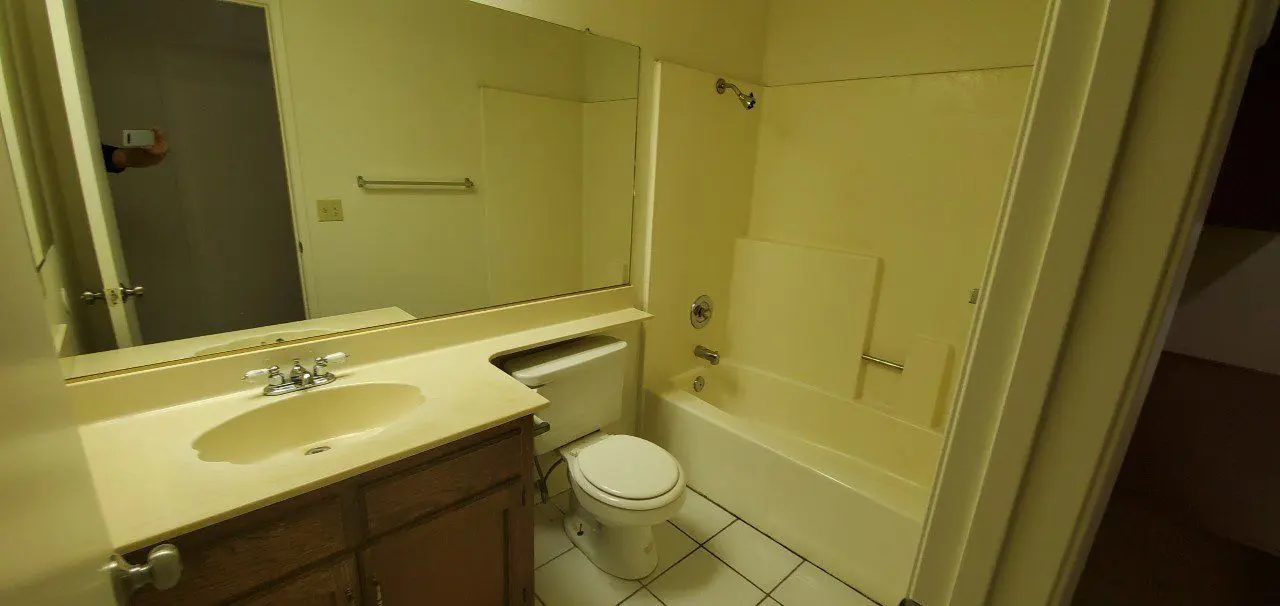 Small bathroom with bathtub, toilet, and sink under a large mirror.