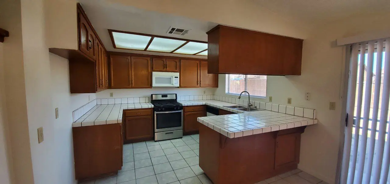 Modern kitchen with wooden cabinets and white tiled countertops.