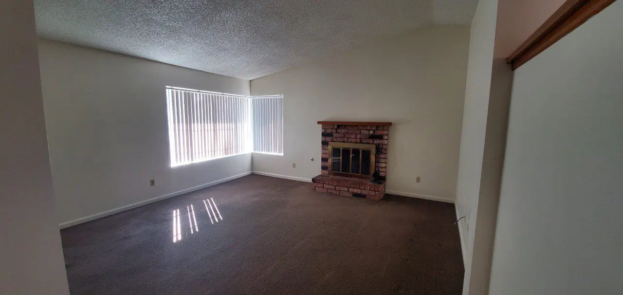 Empty living room with carpet and brick fireplace.