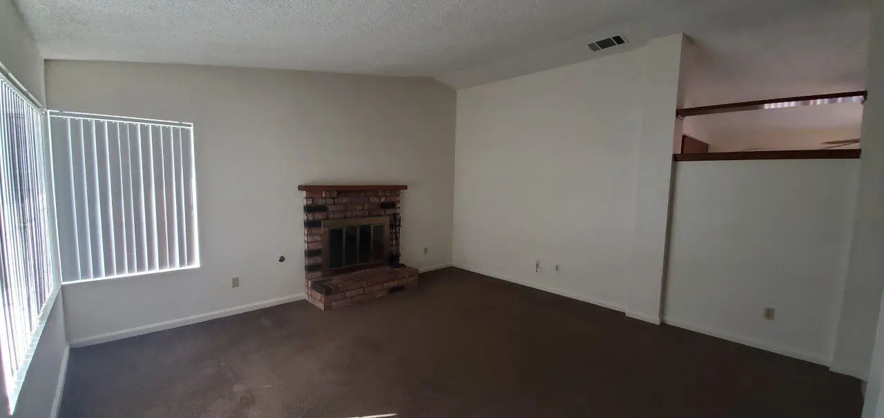 Empty room with carpet and brick fireplace on white walls.