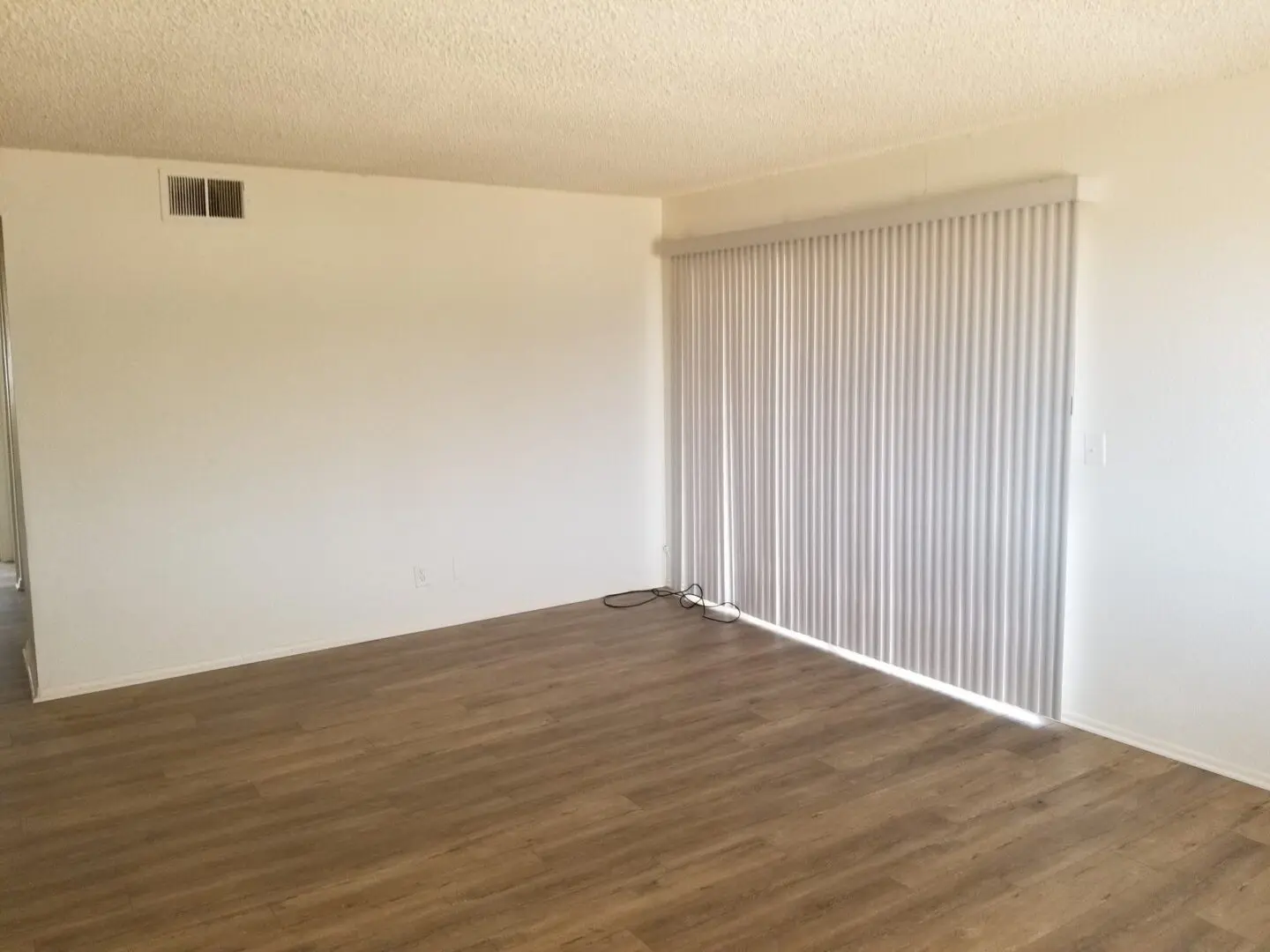 Empty room with wooden floor and vertical blinds.