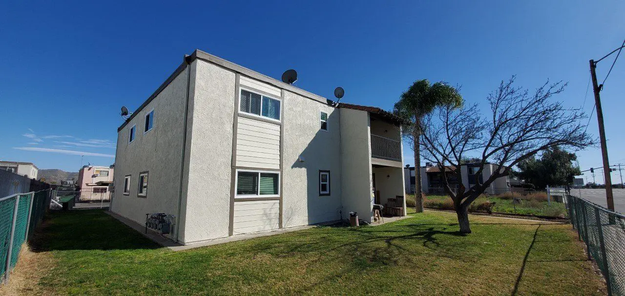 A two-story white apartment building with satellite dishes and a grassy lawn.