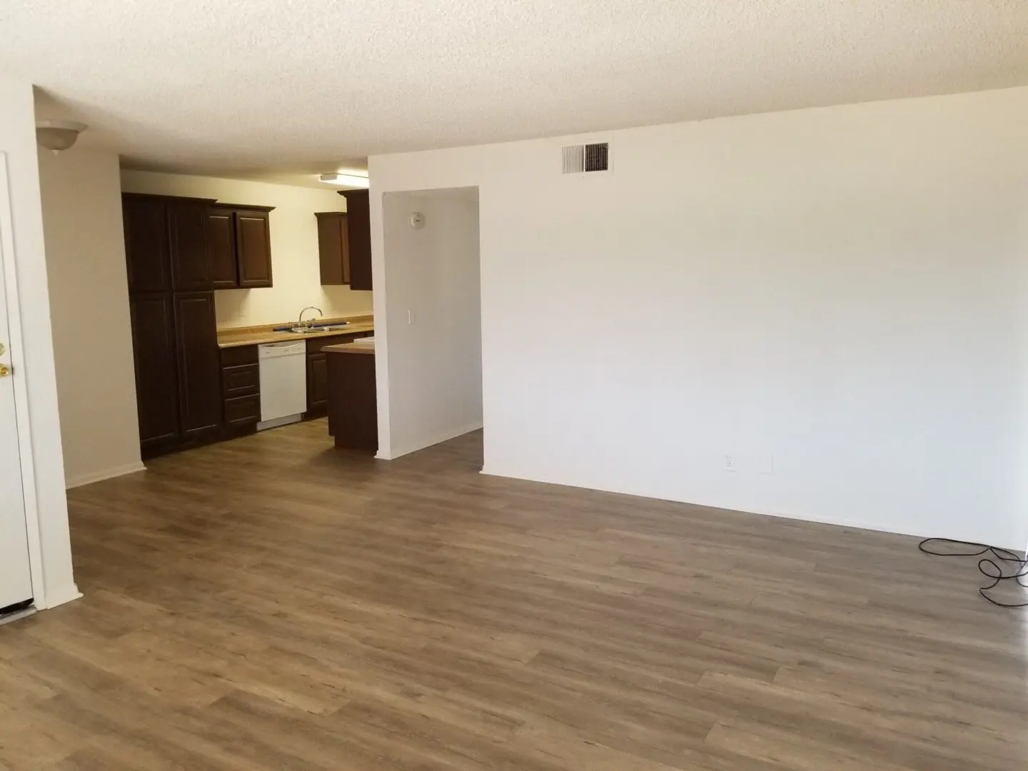 Empty room with wooden floor and kitchen area.