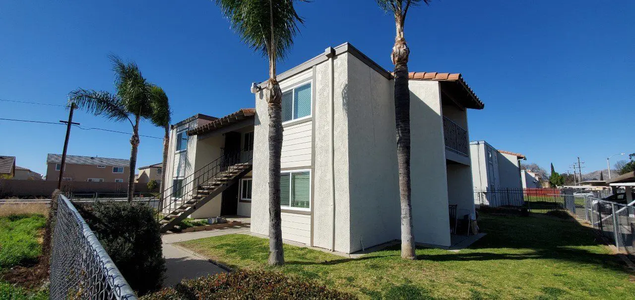 Exterior view of a two-story residential building with palm trees and clear blue sky.