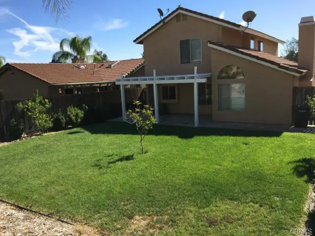 Backyard with green lawn and covered patio in sunny weather.