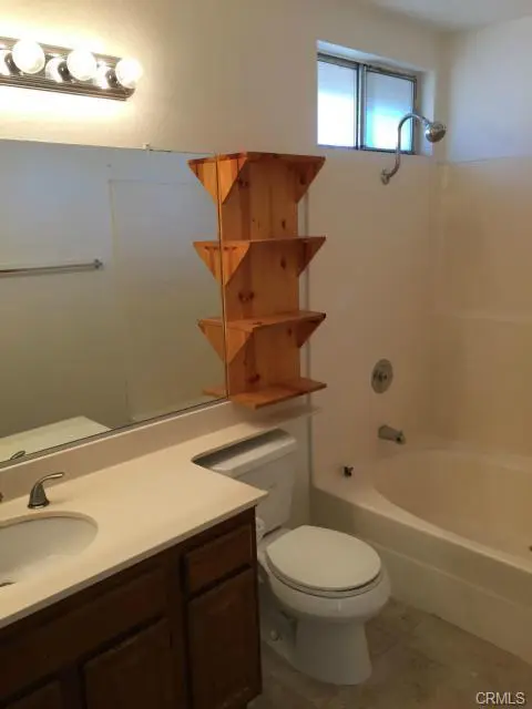 Clean bathroom with wooden shelving above the toilet.