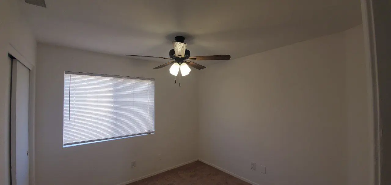 Empty room with ceiling fan and window covered by blinds.