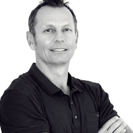 Black and white portrait of a man with crossed arms and a slight smile.