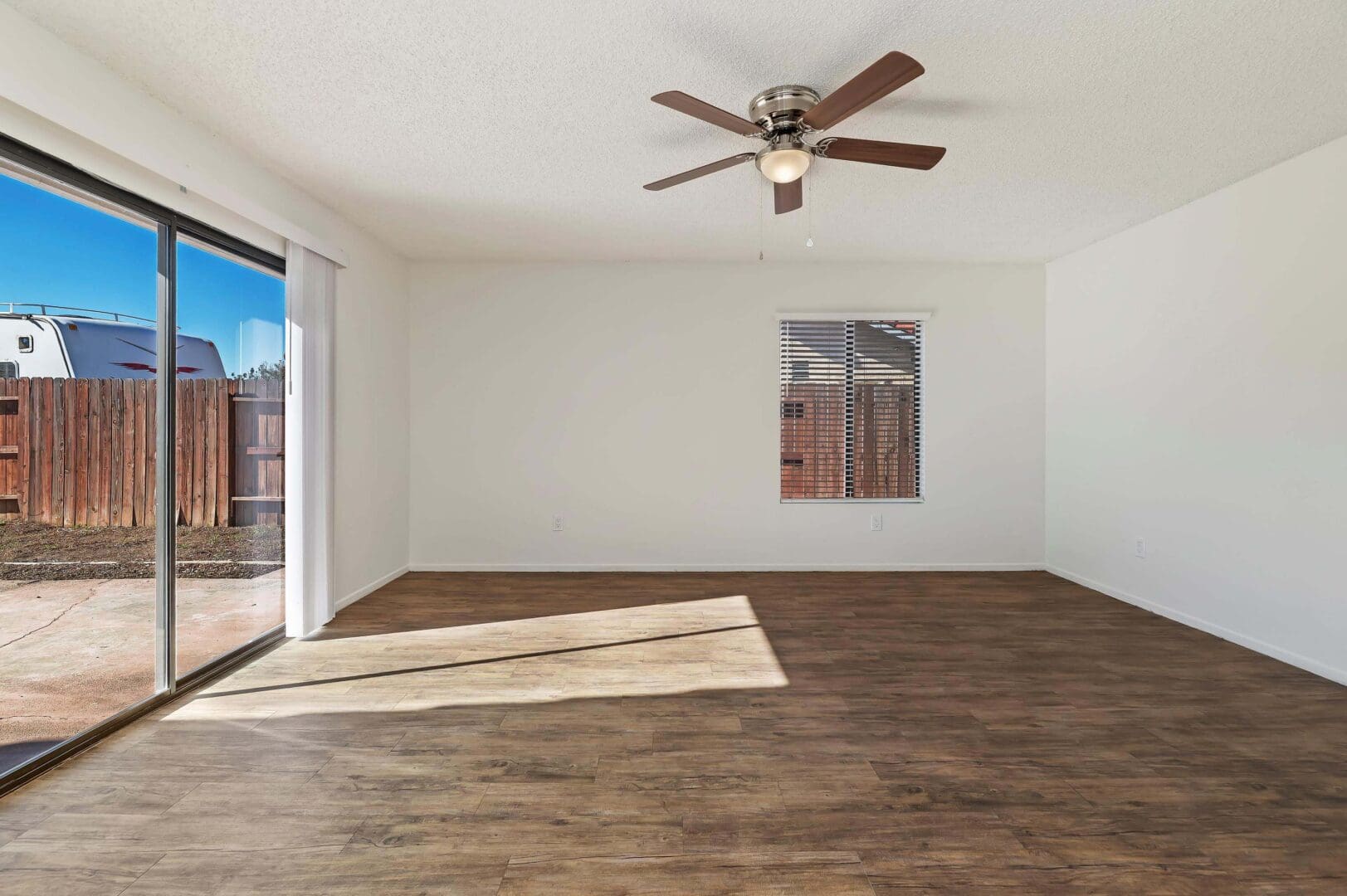 Empty room with wooden floor and fan.